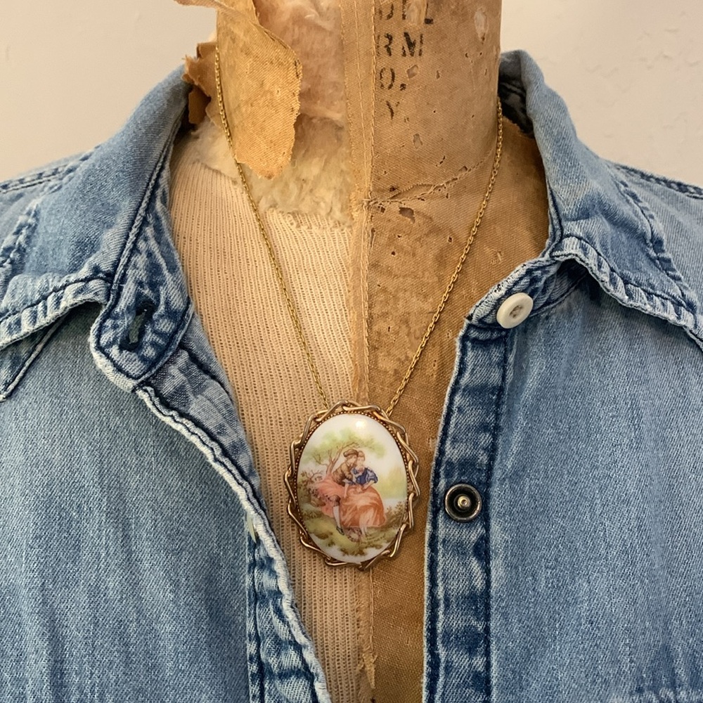 Vintage porcelain brooch w/painted courting couple, gold metal chained bezel.